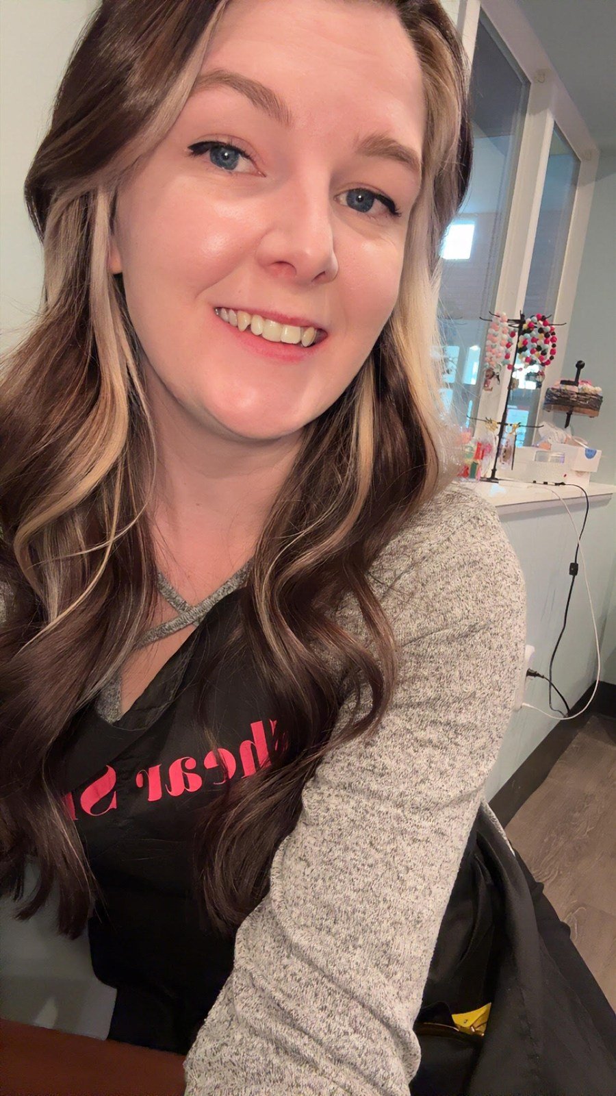 Beth smiling with long wavy brown hair and blonde face-framing highlights