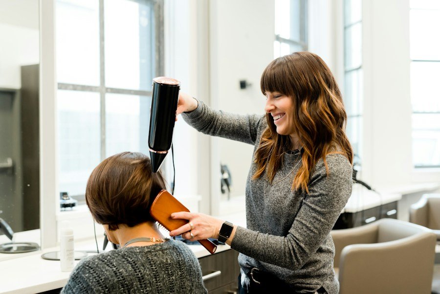 Stylist blow-drying a client’s short brown hair with a dryer and brush