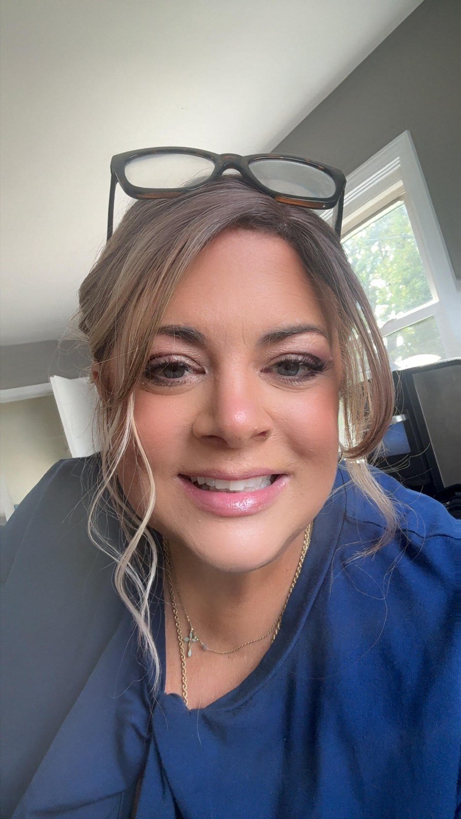 Pam smiling with highlighted brown hair and glasses resting on her head