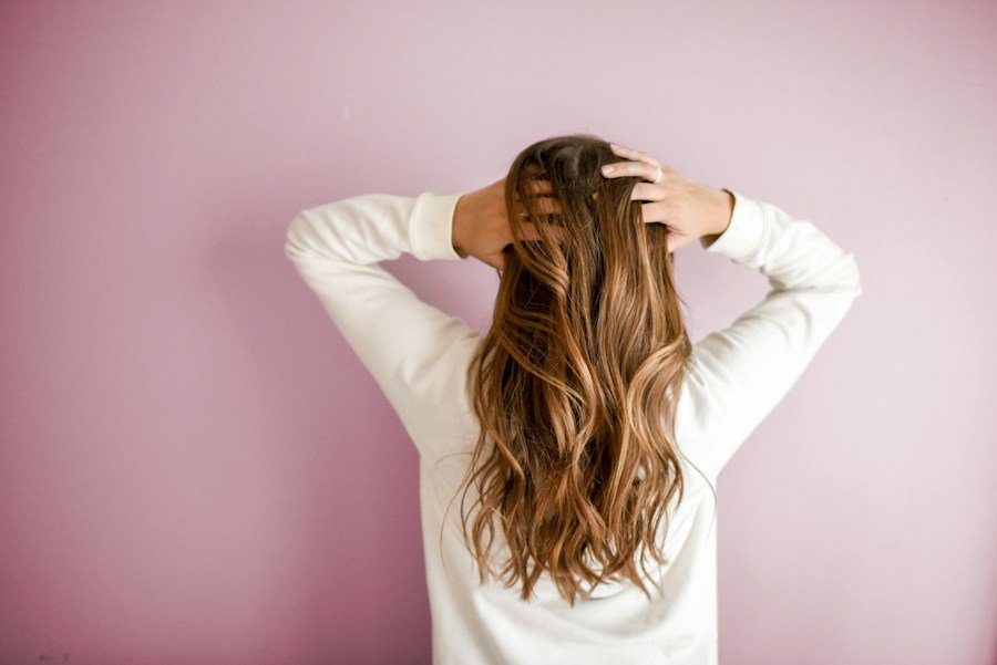 Back view of long, wavy brown hair with golden ends against a pink background